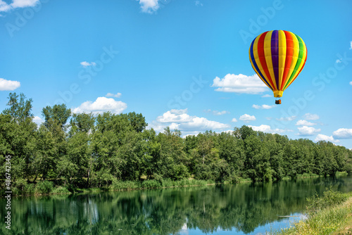 A beautiful landscape of the river surrounded by trees and a hot air balloon on a sunny summer day under blue sky.
