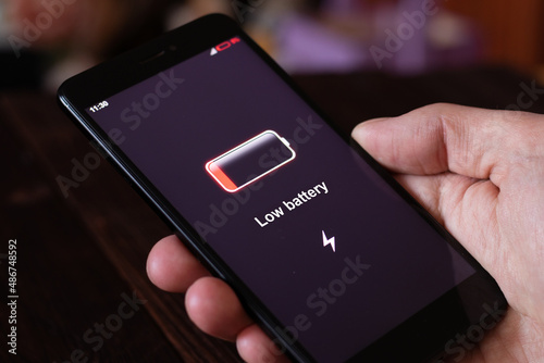 Energy concept: Man hand hold smartphone with low battery. All screen graphics are made up