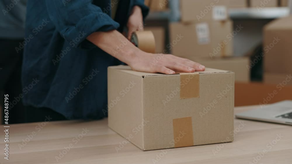 Cropped view of the caucasian man standing at the table and packing parcels with scotch tape attentively. Post service and small business concept. Cropped view of the caucasian man standing at the table and packing parcels with scotch tape attentively. Post service and small business concept.