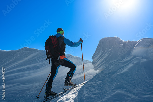 a ski alpinist walks through a snowdrift at the top of a hill. 