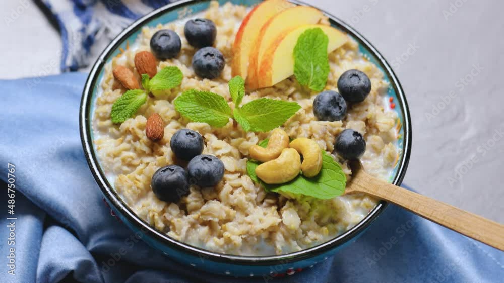 Oatmeal porridge with berries, nuts and honey on gray background. Oatmeal with blueberries, apple slices and fresh mint in bowl. Healthy food concept Oatmeal porridge with berries, nuts and honey on gray background. Oatmeal with blueberries, apple slices and fresh mint in bowl. Healthy food concept
