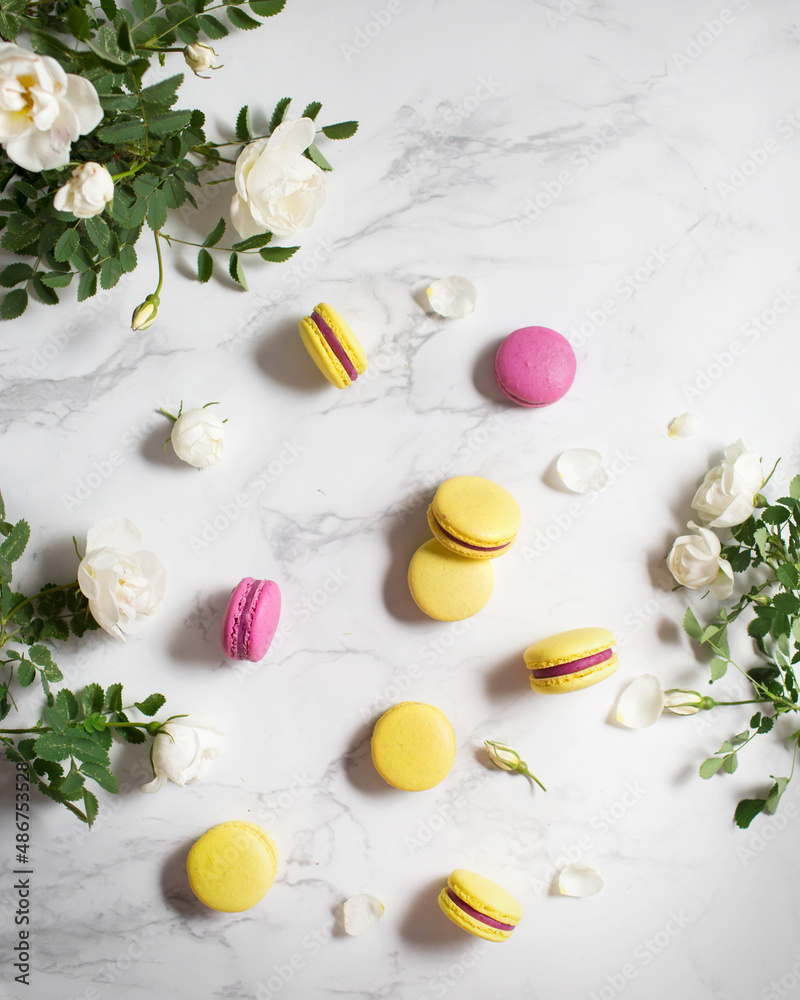 Macaroons and flowers. French food. Yellow and pink macaroons on a marble table. French dessert and white flowers. Macaroons and flowers. French food. Yellow and pink macaroons on a marble table. French dessert and white flowers.