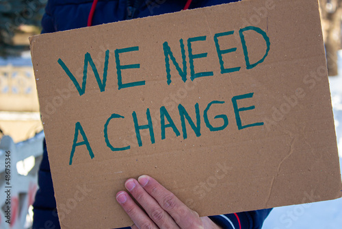 Hand holding cardboard with we need a change text.