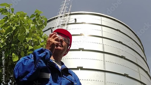 Worker in blue overalls and eyeglasses wearing red hardhat, using walkie talkie radio at an oil refinery HD 1080p