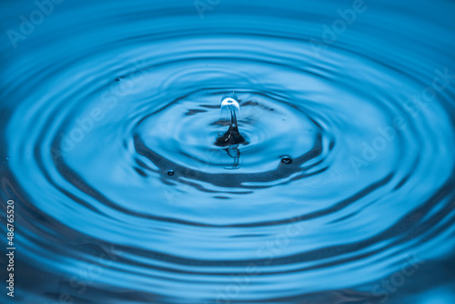 Beautiful view of drops making circles on blue water surface isolated on background.