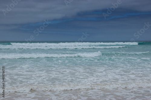 The turquoise, blue and green waves of the sea hit the white sands of the beach at Tortuga Bay, Galapagos Islands.