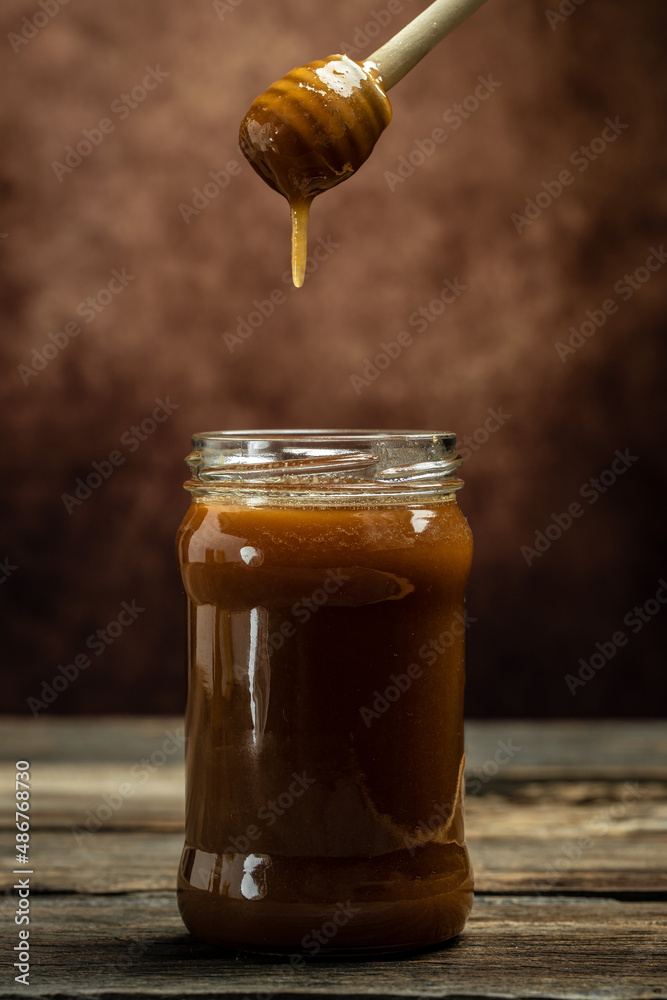Honey jar and wooden spoon in jar. Bees produce fresh, healthy, honey. Honey background. Beekeeping concept Honey jar and wooden spoon in jar. Bees produce fresh, healthy, honey. Honey background. Beekeeping concept