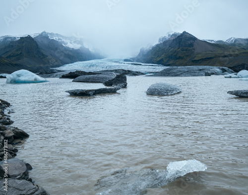 Glacier tongue slides from Vatnajökull icecap or Vatna Glacier near subglacial Öræfajökull volcano, Iceland. Glacial lagoon with ice blocks and surrounding mountains.