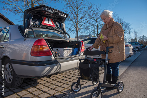 Senior woman with rollator loading foot in car trunk