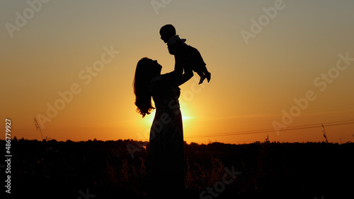 Unrecognizable family silhouette at sunset, happy mother throws up her baby, motherly love