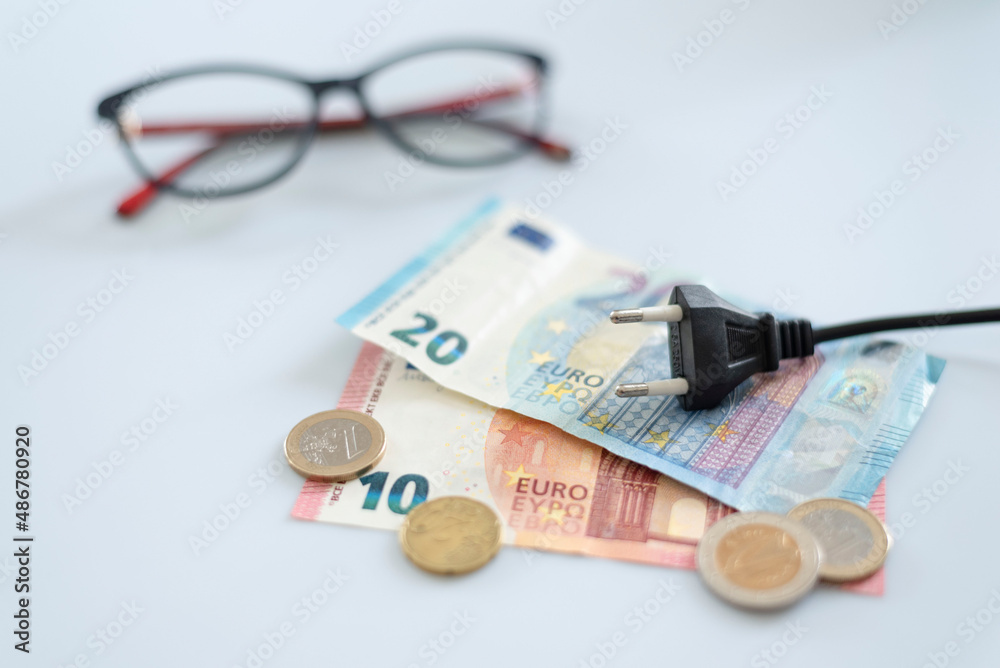 Black electric cap on euro banknotes and various coins, glasses in the background. Increased cost of electricity . Payment of electricity bills. Increasing the concept of electricity prices. Black electric cap on euro banknotes and various coins, glasses in the background. Increased cost of electricity . Payment of electricity bills. Increasing the concept of electricity prices.