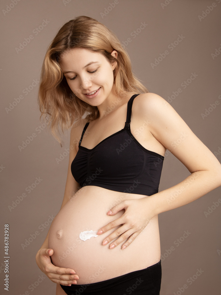 Woman standing and touching with hands her naked big belly. Isolated on gray background. Emotional loving pregnancy time - 37 weeks. Baby expectation. Love, happiness and safety concept. Closeup Woman standing and touching with hands her naked big belly. Isolated on gray background. Emotional loving pregnancy time - 37 weeks. Baby expectation. Love, happiness and safety concept. Closeup