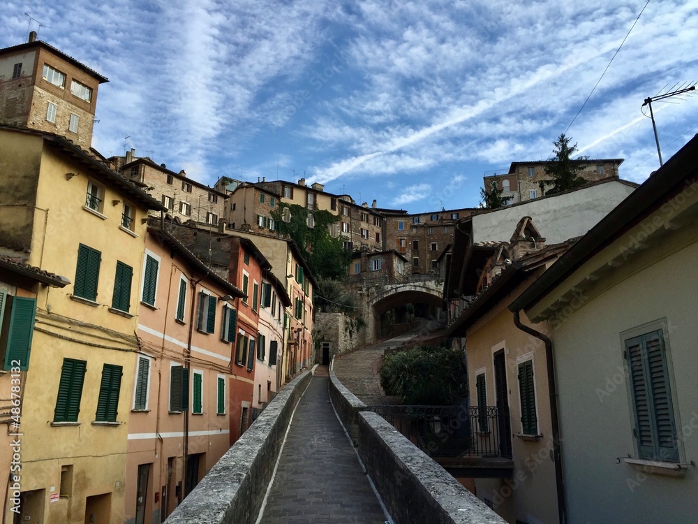 Street of Perugia, Umbria. Heart of Italy. Medieval arch, colorful houses. No people. Blue sky. Narrow passage. Medieval aqueduct