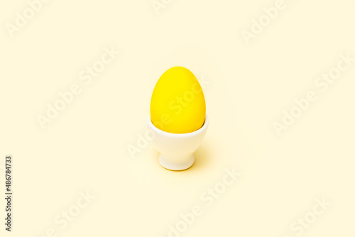 Dyed yellow Easter egg in a white ceramic base on a yellow background. Minimalist style. 