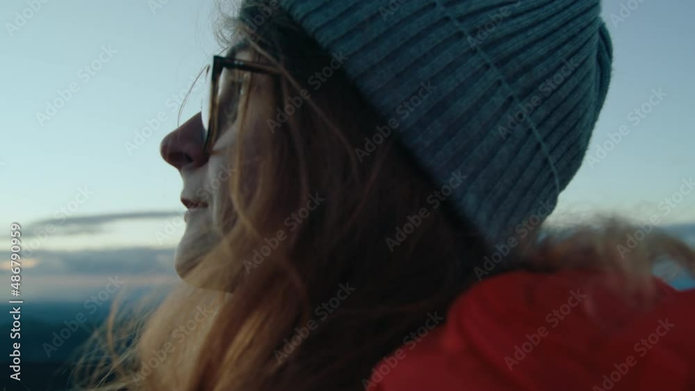 Adult beautiful woman in prescription glasses and knit beanie hat look up at sky during mountain hike. Cinematic inspiring shot of wanderlust travel adventure vibes, travel blogger lifestyle portrait