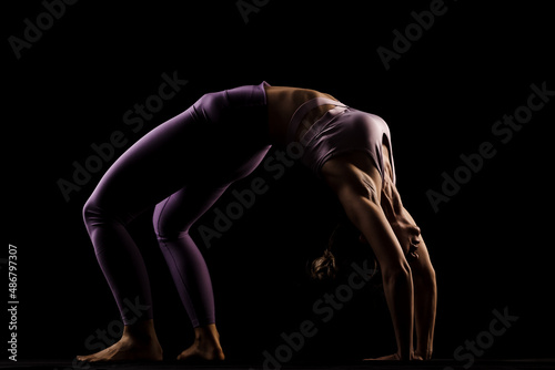 Fit girl practicing yoga in a studio. Half silhouette side lit fitness model.