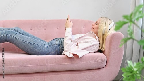 Attractive young blonde woman lying on the couch listeting to music. Relaxing concept	
 photo