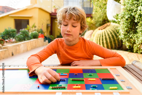 A young elementary school student follows the montessori methodology to learn multiplication using a checkerboard. photo