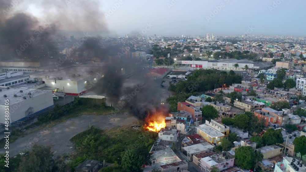 Aerial view of dark smoke rising from a industrial fire, closing in on a large facility - pull back, drone shot