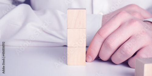 Businessman wearing a blue shirt, arranging the empty wooden blocks with his hands. Which is placed on a white wooden table. Business strategy and action plan. Copy space.