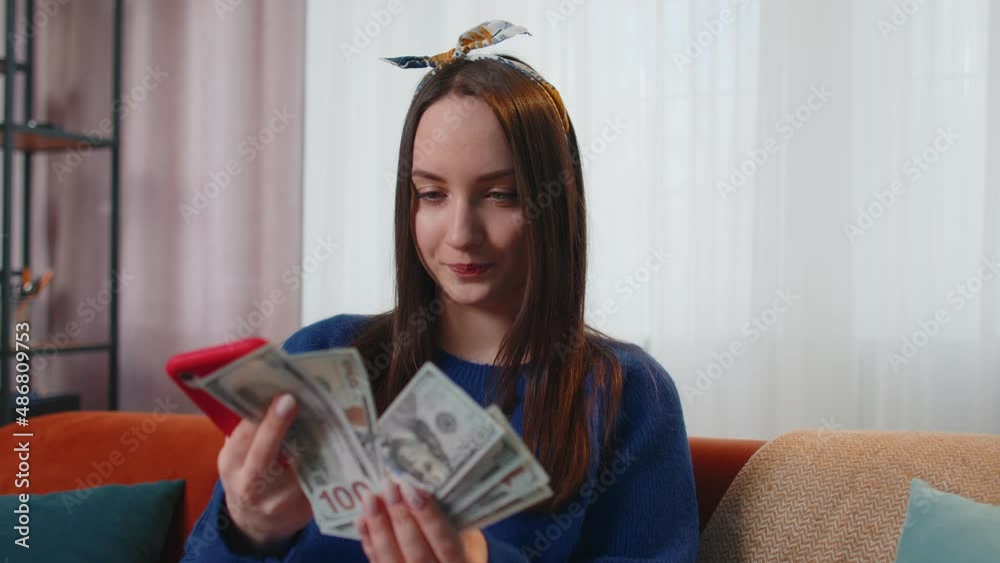 Planning family budget. Smiling happy young woman holding cash money and mobile phone calculate domestic bills at home. Joyful girl satisfied of income and saves money for a planned vacation, gifts Planning family budget. Smiling happy young woman holding cash money and mobile phone calculate domestic bills at home. Joyful girl satisfied of income and saves money for a planned vacation, gifts