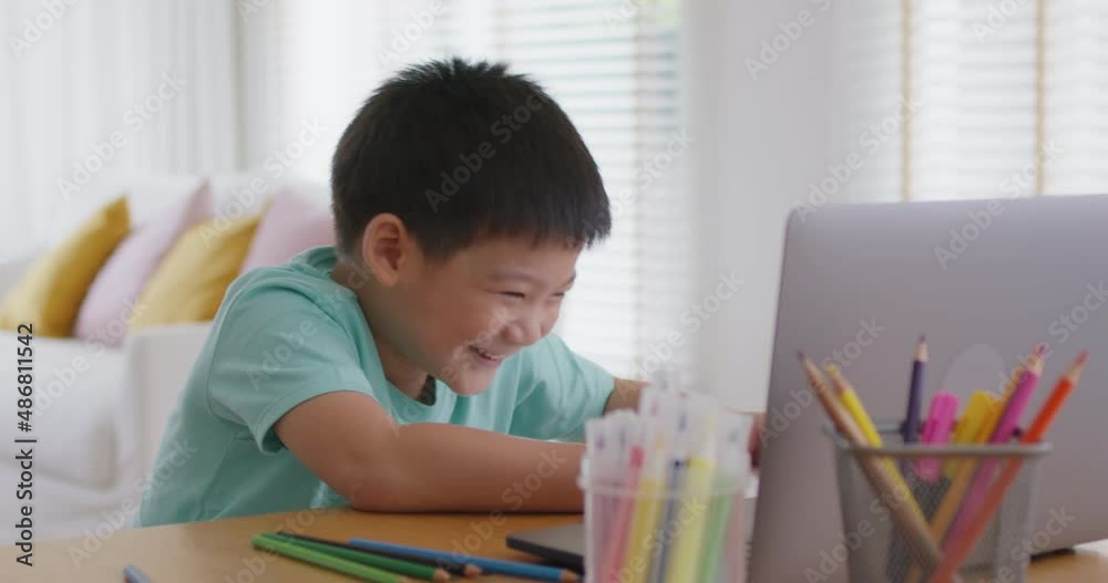 Cute pupil child gen z alpha boy sit talk video call self e-learning lesson on laptop at home table. Asia art school tutor class drawing color pencil in paper watch fun social media upskill kid.     