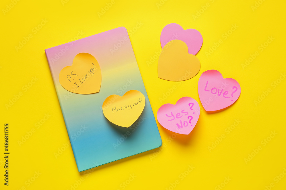 Heart shaped sticky notes with words and notebook on yellow background Heart shaped sticky notes with words and notebook on yellow background