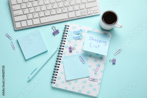 Stationery, cup of coffee, computer keyboard, sticky notes with text SHOPPING LIST and DON'T FORGET on blue background © Pixel-Shot