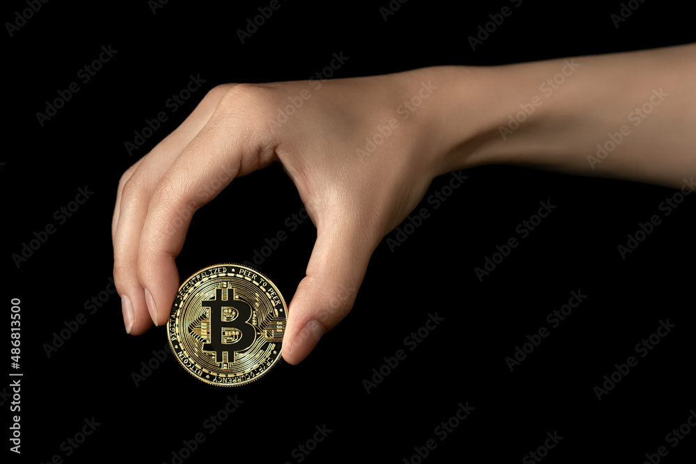 Woman's hand holds a bitcoin in her fingers. Isolated on black background Woman's hand holds a bitcoin in her fingers. Isolated on black background