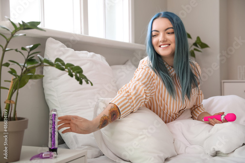 Beautiful young woman taking vibrator from bedside table