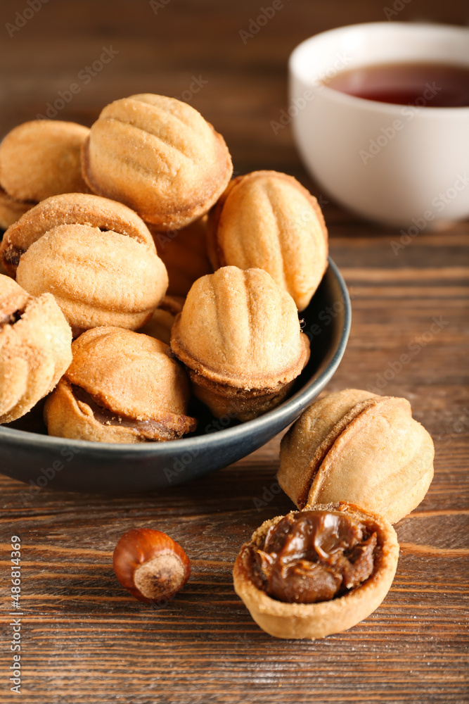 Bowl of tasty walnut shaped cookies with boiled condensed milk on wooden background, closeup