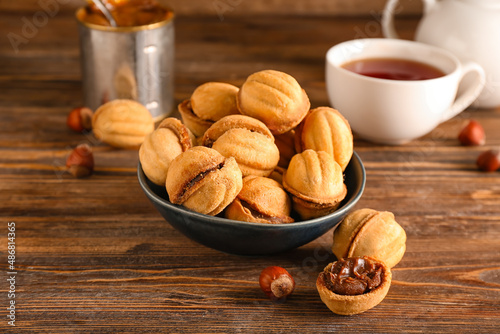 Bowl of tasty walnut shaped cookies with boiled condensed milk on wooden background