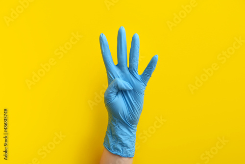 Woman in blue medical glove showing four fingers on yellow background