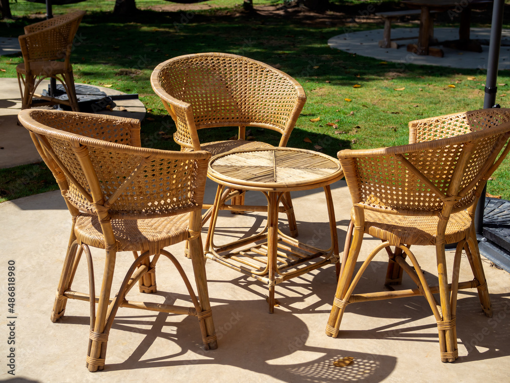 Fototapeta premium Empty rattan furniture, outdoor garden weave table set with round table and three chairs on the green concrete floor in the green yard, simple design.