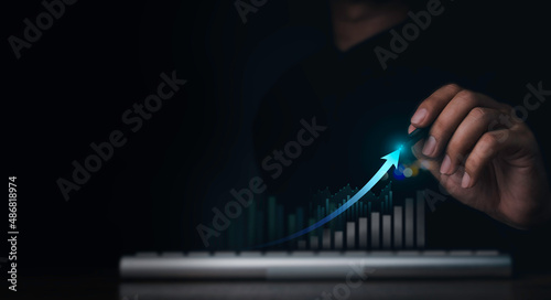 Investment technology, financial, return on investment - ROI concepts. Increasing arrow, the exponential curve of progress in business performance over charts draws by pen in hand on dark background. photo