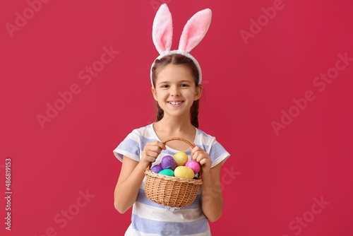 Funny little girl with bunny ears and Easter basket on color background