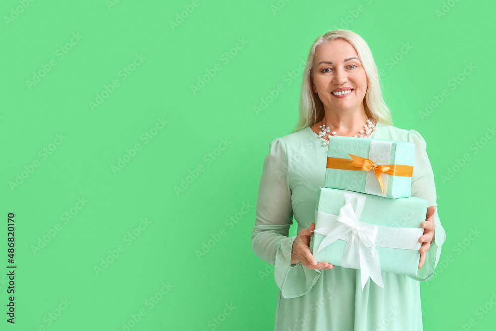 Fashionable mature woman holding stack of gift boxes on green background. International Women's Day celebration Fashionable mature woman holding stack of gift boxes on green background. International Women's Day celebration