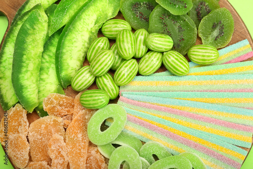 Wooden board with different sweets for St. Patrick's Day celebration on green background