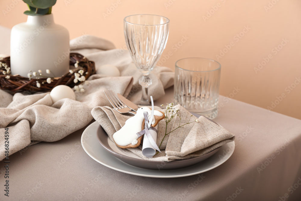 Dining table for Easter celebration with cookie in shape of bunny near beige wall Dining table for Easter celebration with cookie in shape of bunny near beige wall