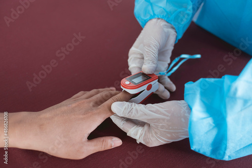 A nurse in PPE gear inserts an Oximeter on a patient's index finger. Checking blood oxygen or SpO2 levels. At the emergency ward of a hospital.