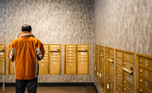 Man standing at mailroom inside apartment, depth of field. People waiting for getting letter at letterbox. Mailman or receiver concept, deliver or receive mail from metal storage by room number.