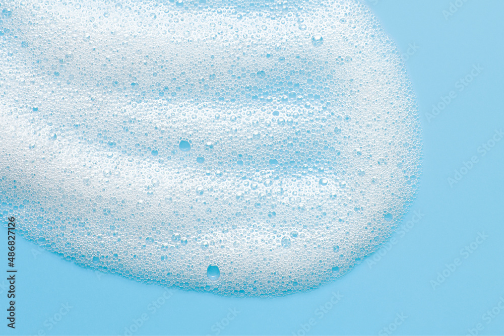 Cosmetic foam bubbles on blue background. Cleanser, face wach, hair shampoo soap suds texture. Abstract foamy cleansing product macro - obrazy, fototapety, plakaty 
