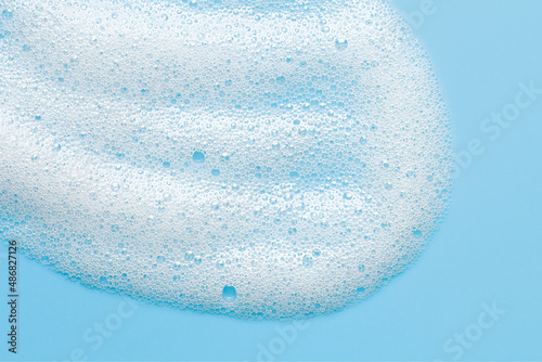Cosmetic foam bubbles on blue background. Cleanser, face wach, hair shampoo soap suds texture. Abstract foamy cleansing product macro