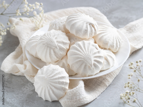 Airy Russian marshmallow dessert zephyr. Meringue dessert on a white plate next to flowers. Selective focus. Light background.