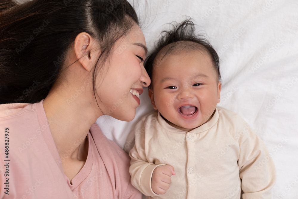 New asian mom playing to adorable newborn baby on bed smiling and happiness at home.Mom talking with infant baby and kissing on baby cheek with love.Baby and Mother day concept New asian mom playing to adorable newborn baby on bed smiling and happiness at home.Mom talking with infant baby and kissing on baby cheek with love.Baby and Mother day concept
