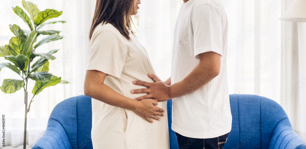 Fototapeta premium Romantic sweet asian couple husband hugging and smiling beauty asian pregnant wife.Man expecting with woman pregnancy hold to baby in belly at home