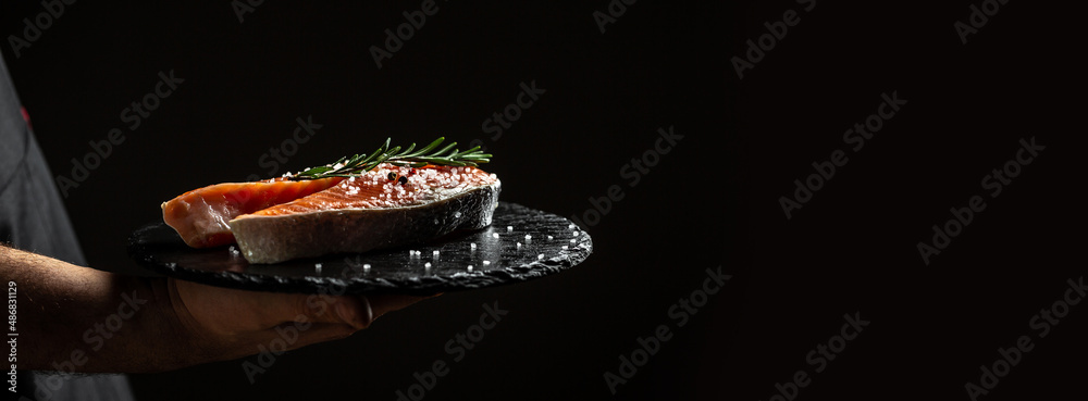 chef prepares salmon steak, process of sprinkling with spices and salt in a freeze motion, marinating salmon fish, adds herbs, seasoning. Long banner format, top view chef prepares salmon steak, process of sprinkling with spices and salt in a freeze motion, marinating salmon fish, adds herbs, seasoning. Long banner format, top view