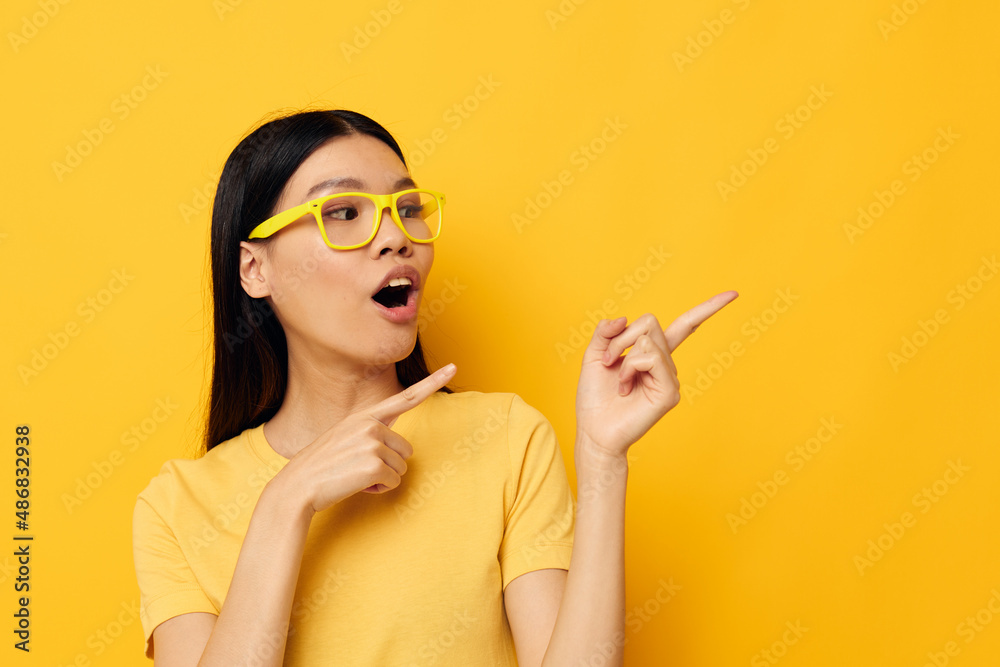 Obraz premium Charming young Asian woman in yellow t-shirts with glasses posing fashion yellow background unaltered