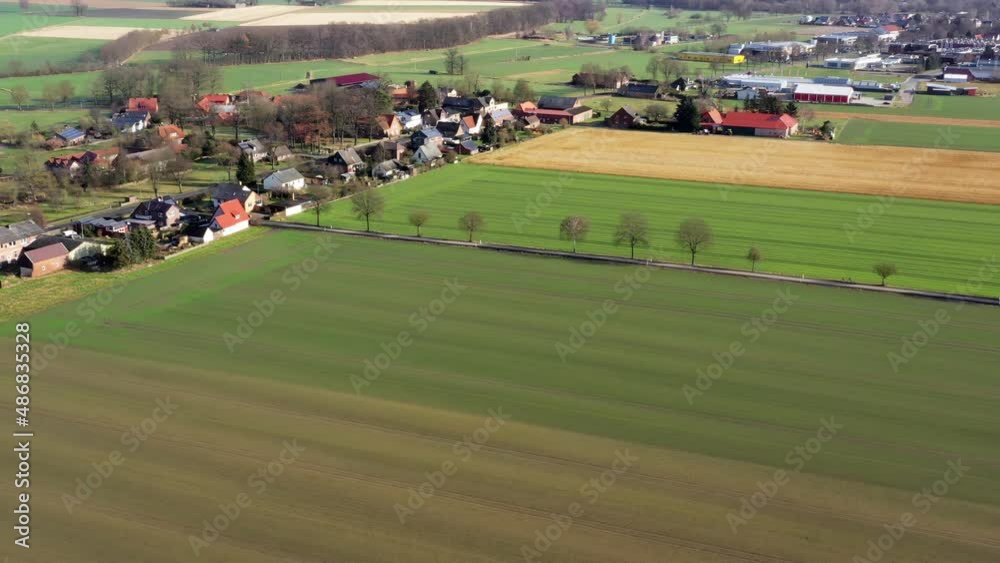 Aerial view of flight over green farmland with a country road with trees and houses of a village in the background Aerial view of flight over green farmland with a country road with trees and houses of a village in the background