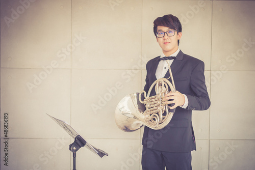 Portrait of young musician with suit form playing horn in music room.